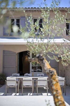A building with a terrace, outdoor seating, and a tree in the foreground. - Provençal country house - Swimming pool - Sleeps 9 (Entrecasteaux)