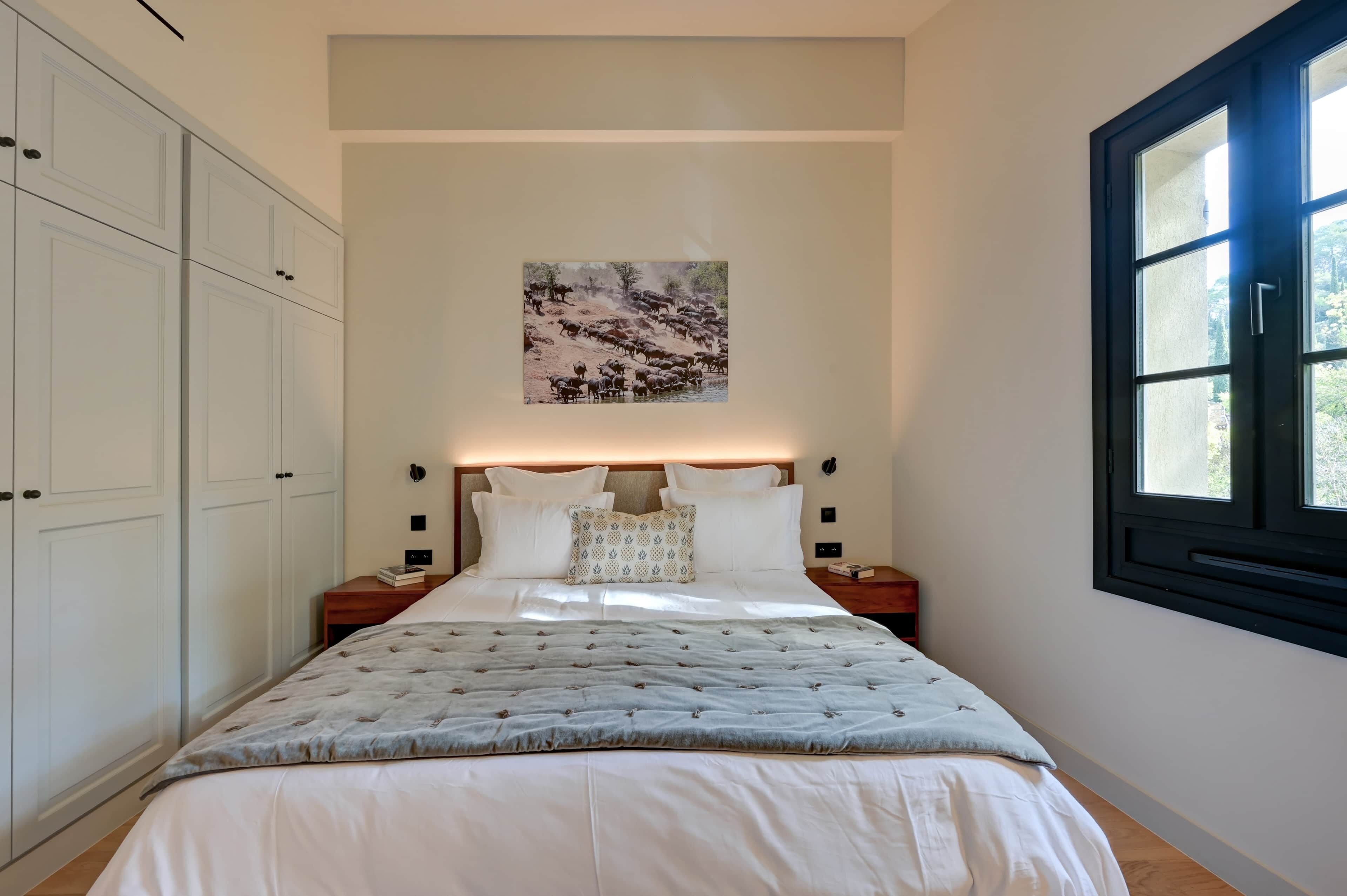 Un dormitorio con una cama grande, paredes blancas, un cuadro y una ventana.