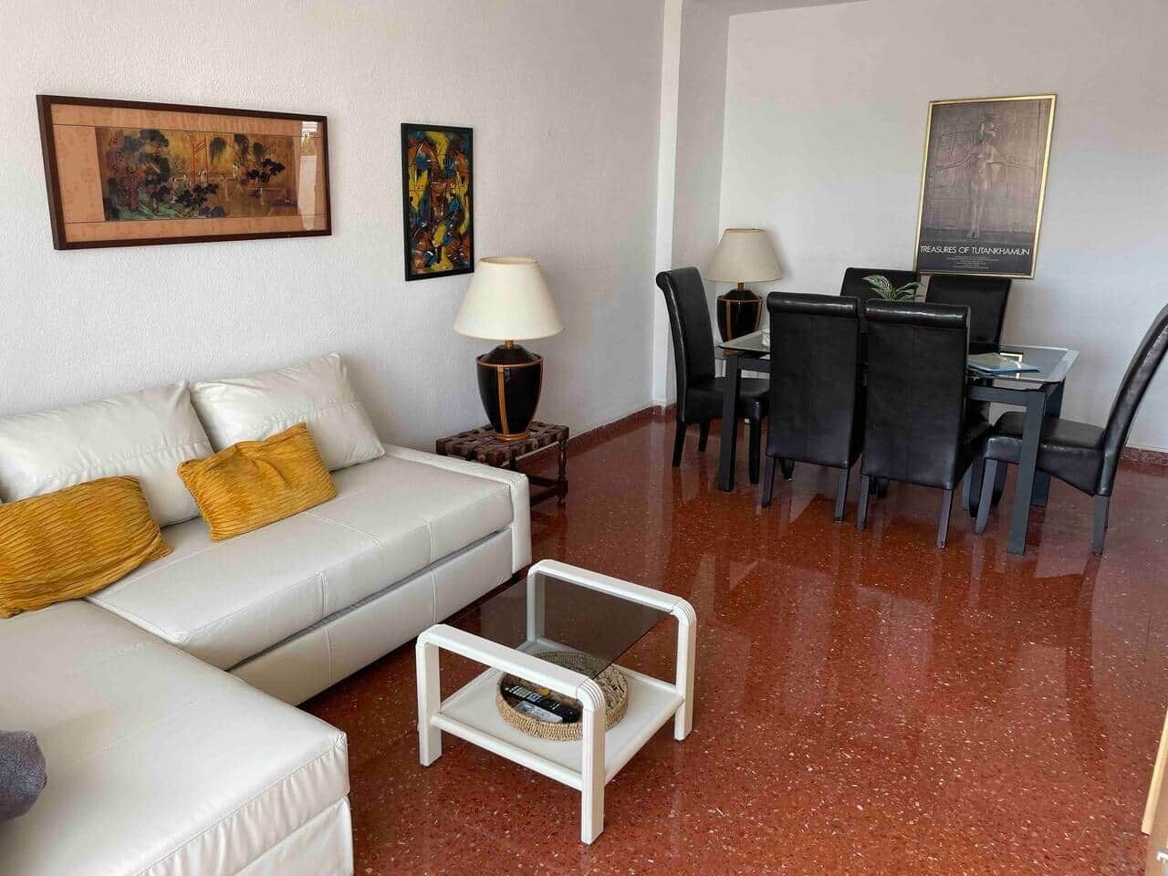 Un salon avec un canapé blanc, une table basse, une table à manger avec des chaises et des œuvres d’art accrochées aux murs.