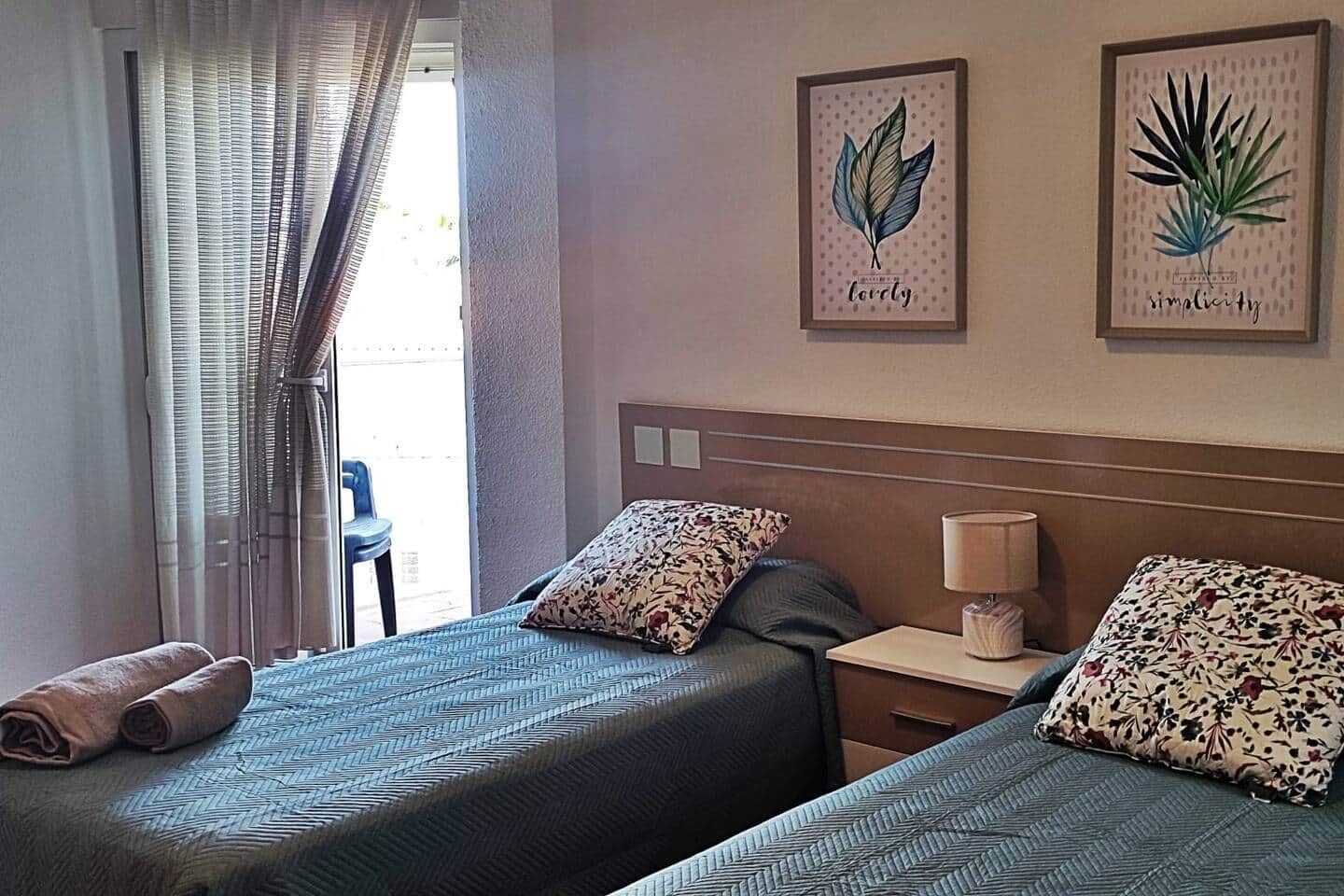 Een hotelkamer met twee bedden, een nachtkastje met een lamp en twee ingelijste kunstwerken aan de muur.