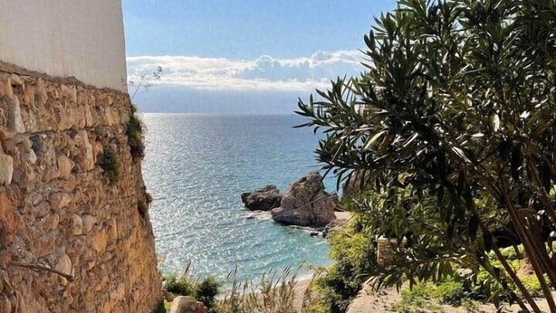 Eine steile Steintreppe führt zu einer Küstenlandschaft mit Blick auf das Meer und Felsformationen.