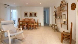 Ein geräumiges Wohnzimmer mit einem modernen Sofa, einer Essecke mit Holzkästen und einem Bücherregal mit Dekorationselementen.