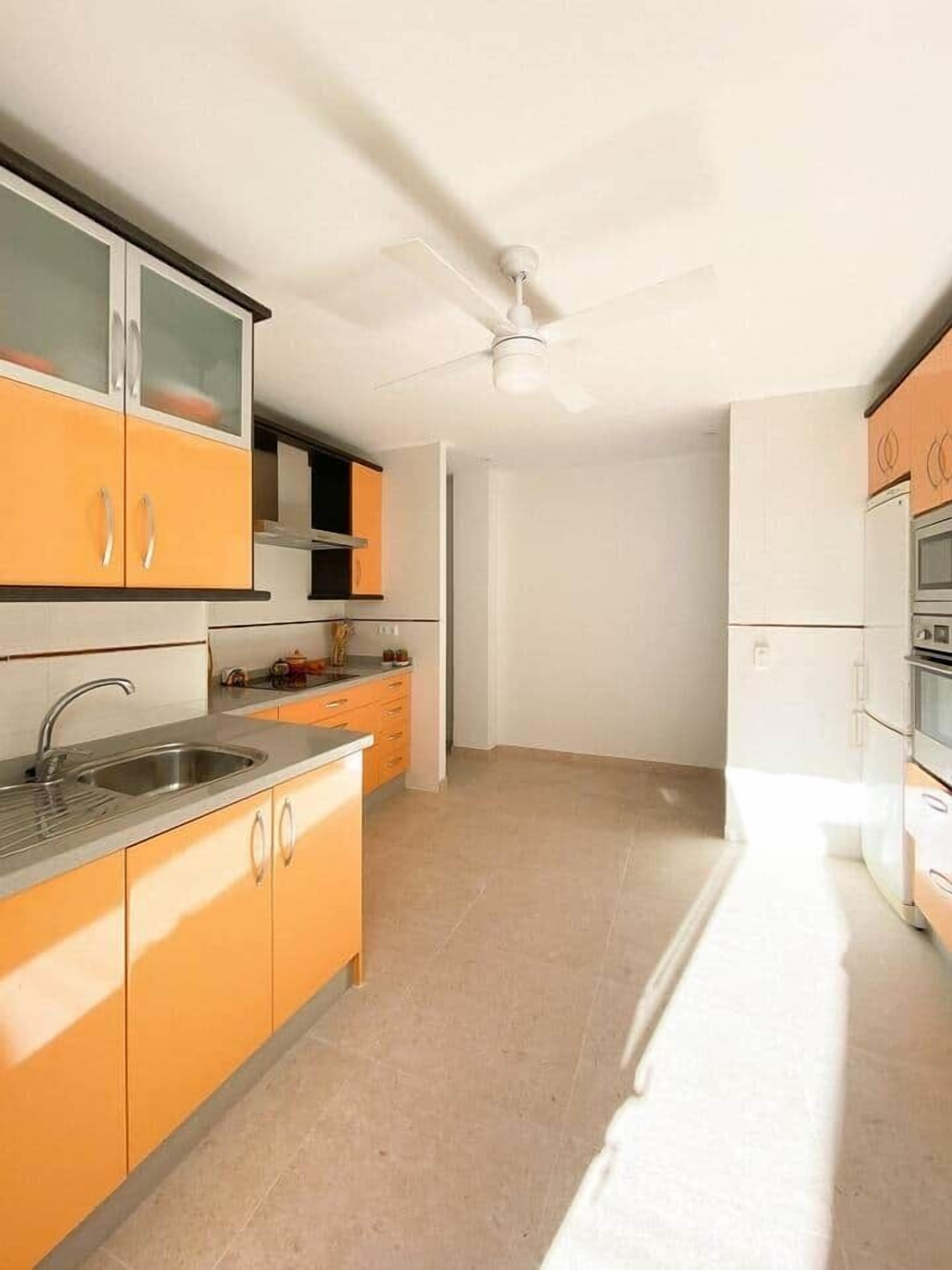Una cocina con gabinetes color naranja, un lavamanos de acero inoxidable y un ventilador de techo.