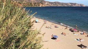 Ein Strand mit badenden und sonnenden Menschen, umgeben von Bergen und blauem Himmel.