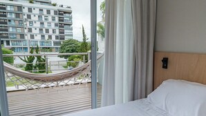 A hotel room with a bed, a view of a cityscape, and a hammock on the balcony. - Casa em Jurerê com 4 quartos - 10 min da praia (Florianópolis)
