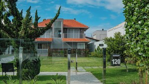 A modern two-story house with a red-tiled roof, a visible mailbox with the number 120, and a well-maintained lawn with various plants. - Casa em Jurerê com 4 quartos - 10 min da praia (Florianópolis)