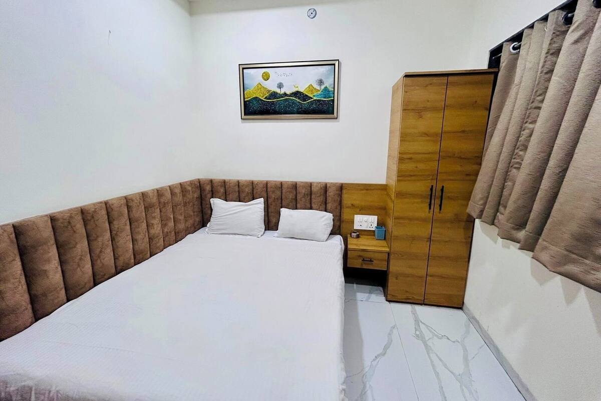 A bedroom with a bed, a wooden wardrobe, a nightstand, and a painting on the wall.