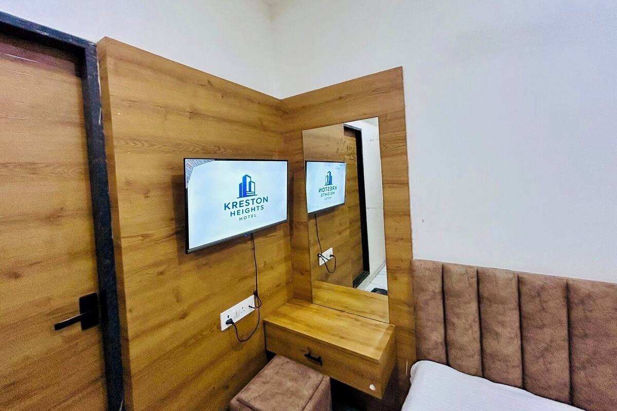 A hotel room with a wooden wall panel, a flat-screen TV mounted on the wall, a wooden bedside table, and a bed with a headboard.