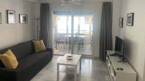 A modern living room with a sofa, a coffee table, a TV, and a balcony with a table and chairs. - Fuentes de Nerja C 2F (Nerja)