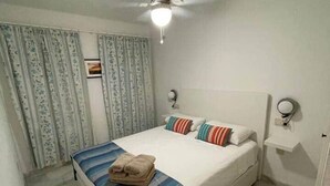 A bedroom with a bed, curtains, a ceiling fan, and a bedside table. - Fuentes de Nerja C 2F (Nerja)