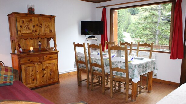 A room with a wooden dining table, chairs, a television, and a window with a view of trees. - 6-person apartment 50 m from the slopes, ideal for enjoying the mountains (VARS)