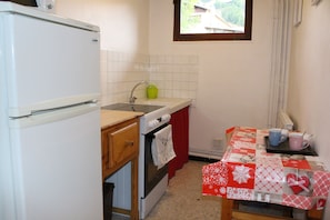 Eine kleine Küche mit Kühlschrank, Spüle, Backofen und Tisch mit rotem und weißem Tischläufer.