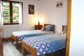 Ein Schlafzimmer mit zwei Holzbetten, einem Nachttisch mit Lampe, einem Fenster mit Vorhängen und einem Heizkörper.