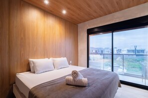 Una habitación de hotel moderna con una cama grande, paneles de madera y vistas a la ciudad a través de un ventanal.