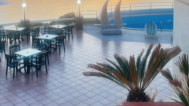 Une terrasse avec des tables et des chaises, une piscine et une vue sur le coucher de soleil.