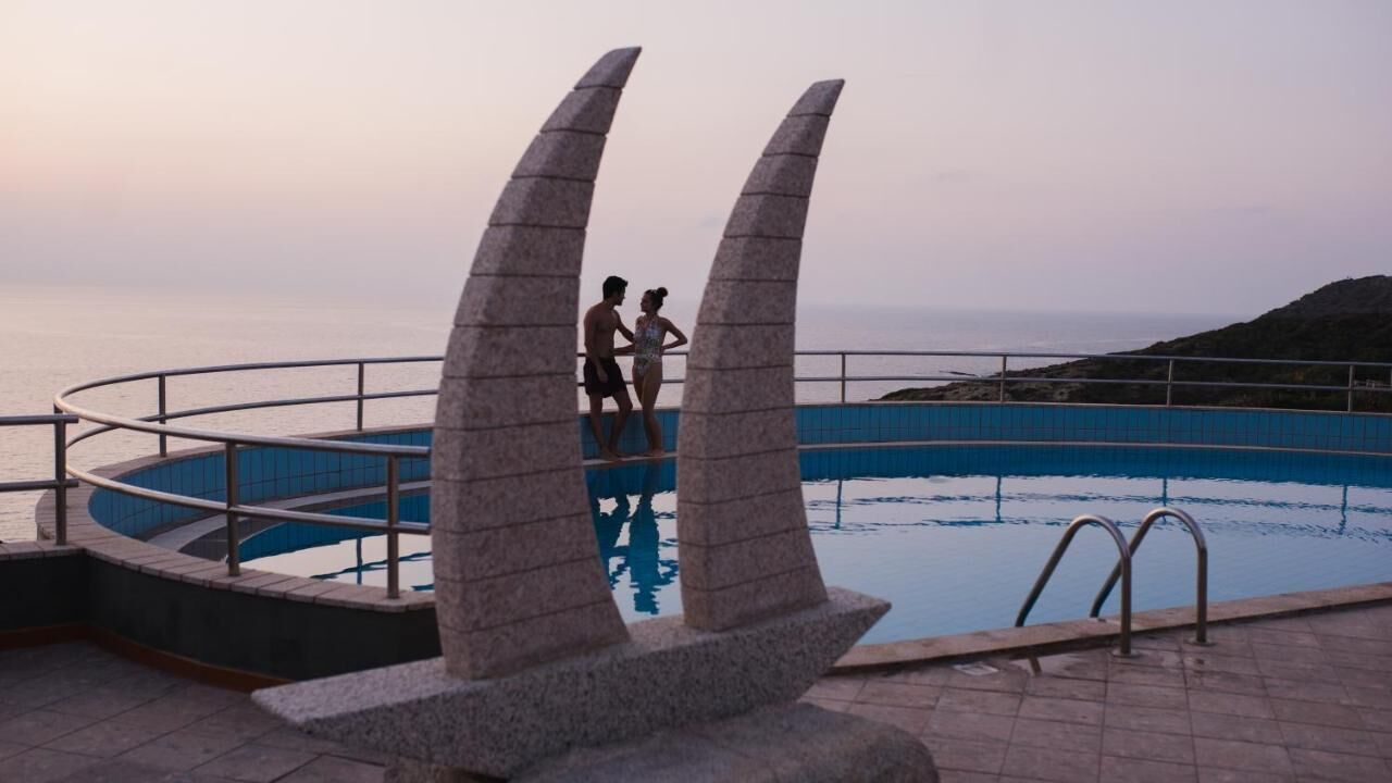Una piscina con dos grandes esculturas de piedra, una barandilla metálica y vistas al mar.