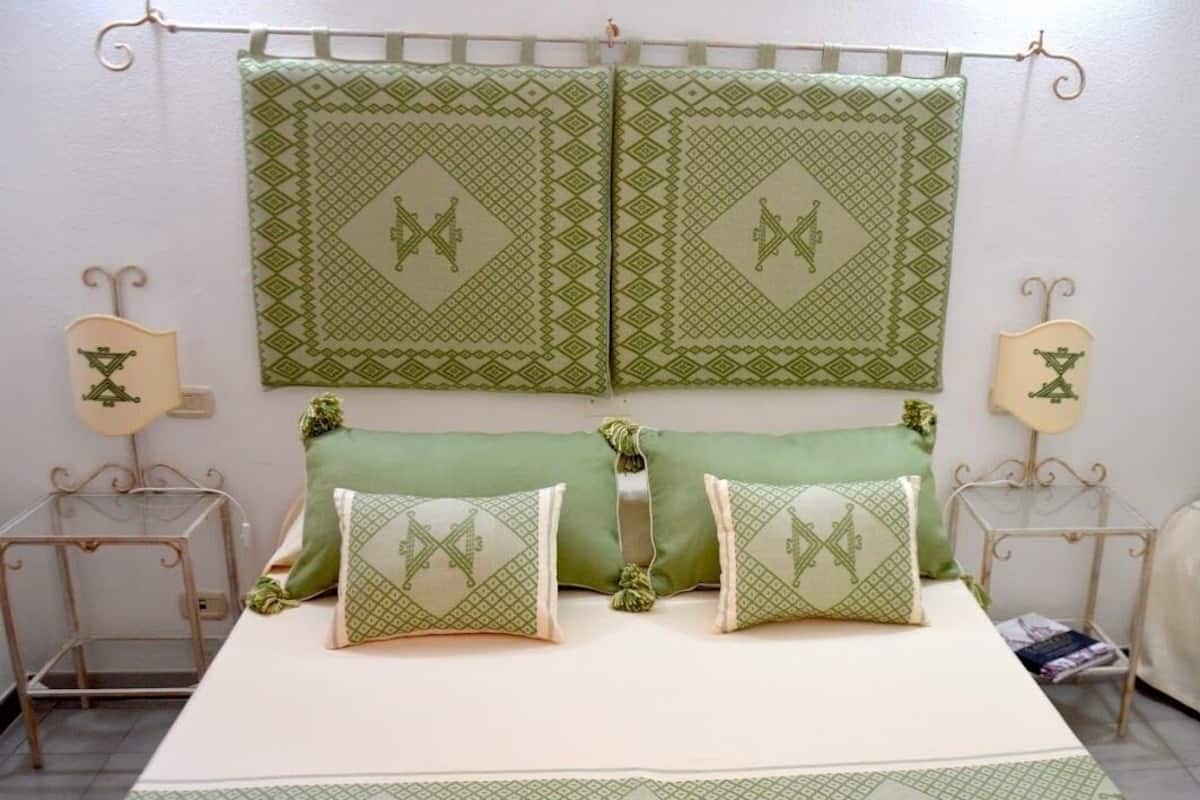 A bed with green bedding, two pillows with a geometric pattern, and a matching green throw.