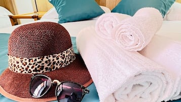 Una cama bien hecha con ropa de cama color turquesa, un sombrero tejido marrón con una banda de estampado de leopardo, gafas de sol y toallas enrolladas.