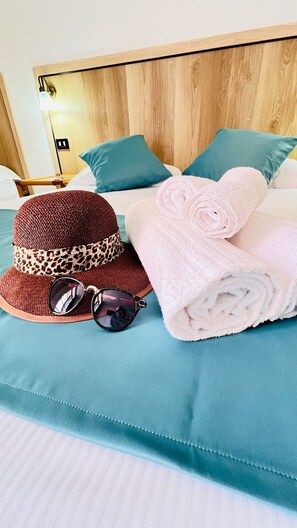 A neatly made bed with teal bedding, a brown woven hat with a leopard print band, sunglasses, and rolled towels. - Zeeva Hotel & Resort (Torre dei Corsari)