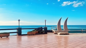 Une terrasse avec vue sur la mer, dotée d’une balustrade, d’un espace salon et de deux lampadaires.