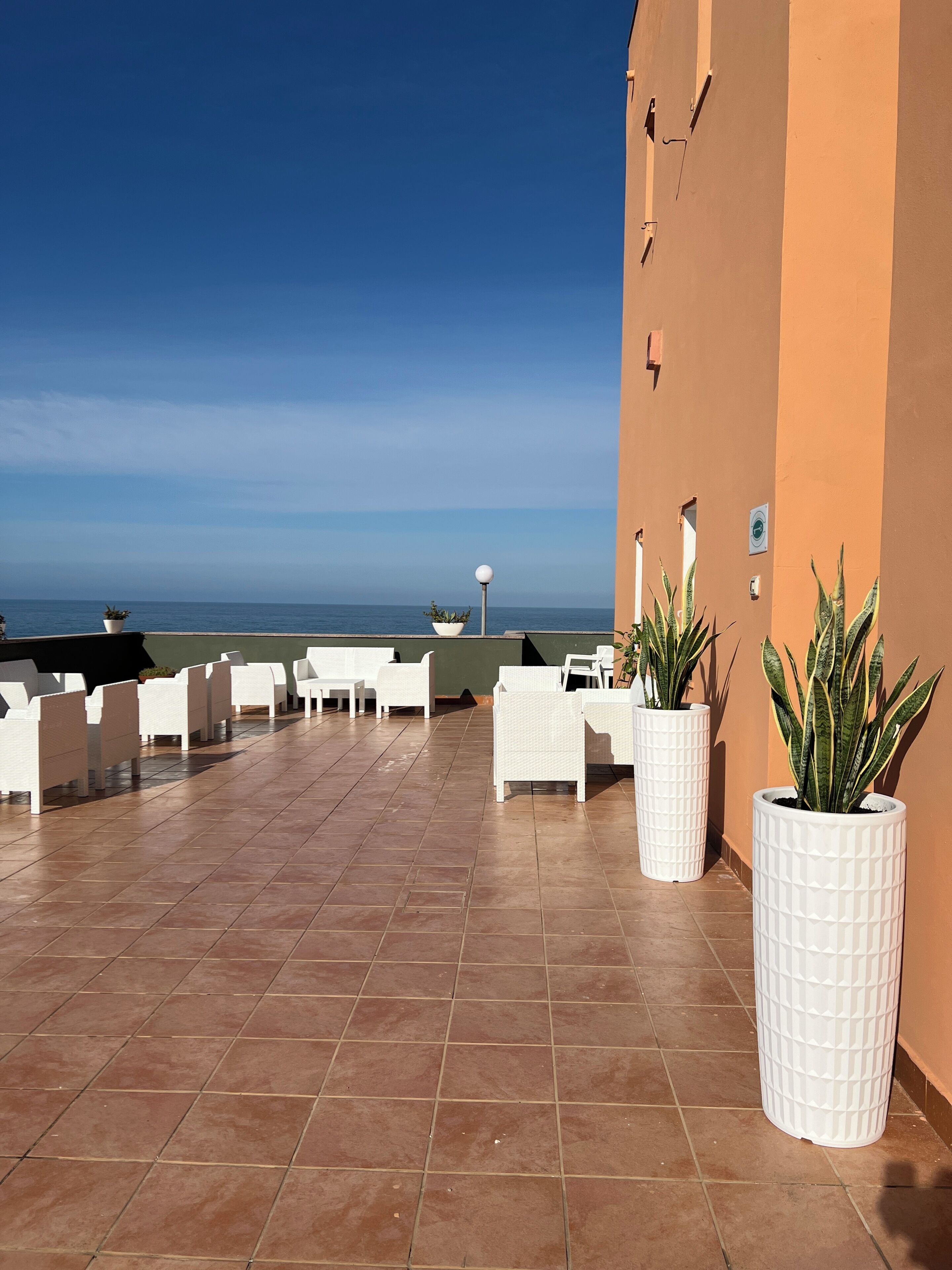 A terrace with white chairs and potted plants, overlooking a body of water.