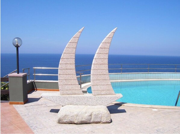 A pool area with a clear view of the ocean, a stone sculpture, and a lamp post. - Zeeva Hotel & Resort (Torre dei Corsari)