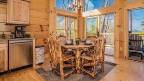 Una cabaña rústica de madera con comedor, que incluye una mesa redonda y sillas de madera natural.