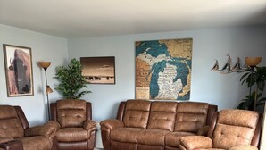 Un salon avec un grand canapé d’angle, une petite table basse ronde et une carte accrochée au mur.