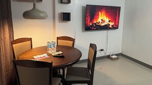 A modern living room with a dining table, chairs, a flat-screen TV displaying a fireplace, and a pendant light. - Cozy Clean Space with Balcony - Near Entrance (Davao City)