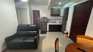 A compact living space with a kitchenette, a black leather sofa, a dining table with chairs, and a wooden door. - Cozy Clean Space with Balcony - Near Entrance (Davao City)