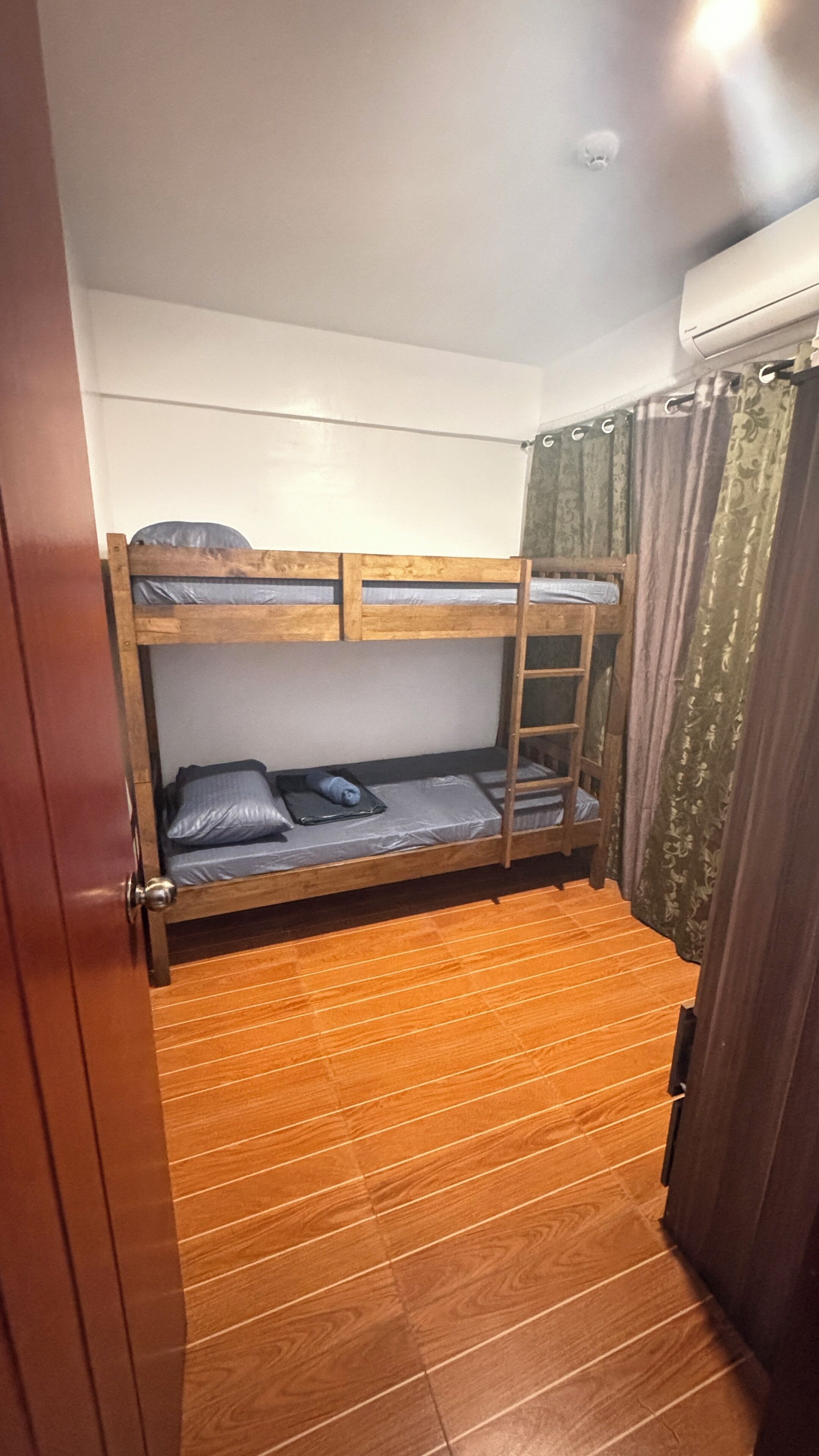 A bunk bed room with a wooden floor, a ladder, and a window with curtains.