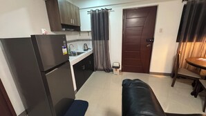 A compact kitchen with a refrigerator, a sink, and a stove. There is a dining table with chairs and a bench. - Cozy Clean Space with Balcony - Near Entrance (Davao City)