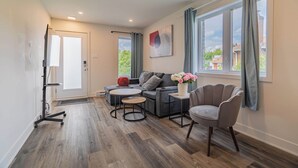 Een moderne woonkamer met een bank, twee ronde tafels, een stoel en een groot raam met gordijnen.