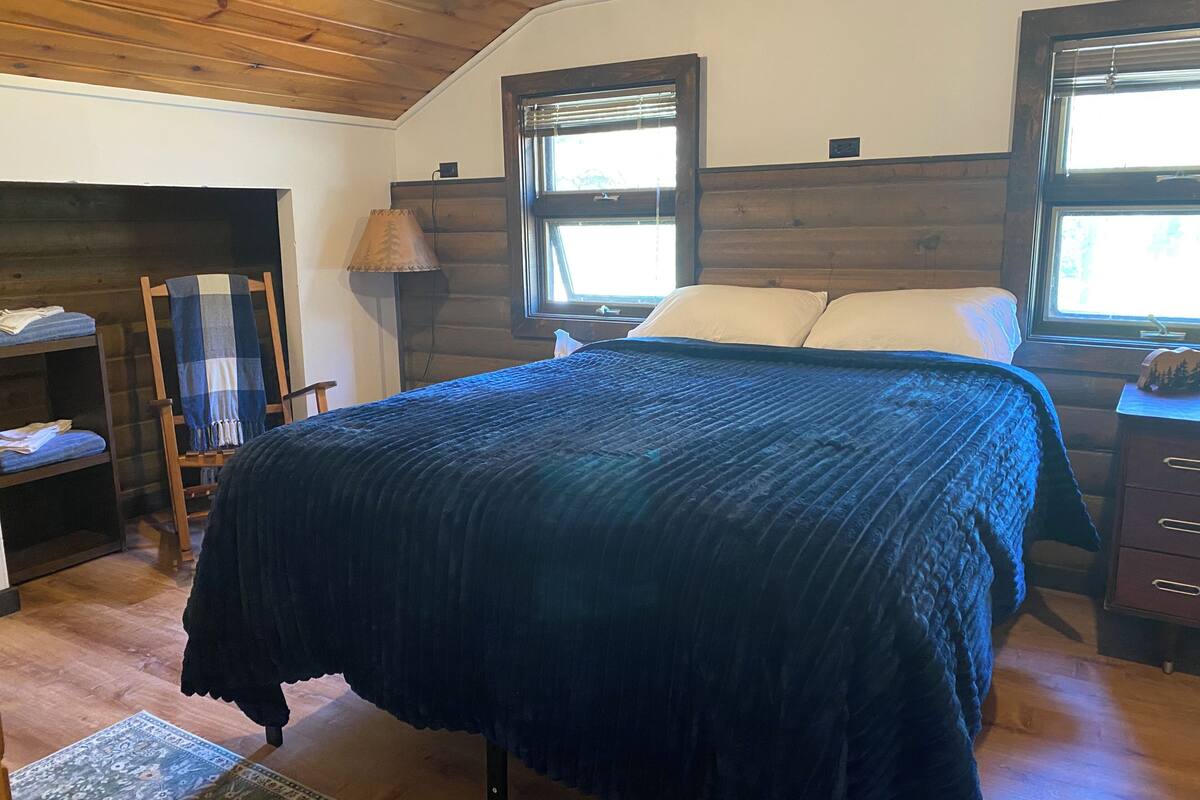 A bedroom with a bed, a nightstand, a lamp, a chair, and a shelf.