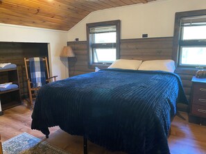 A bedroom with a bed, a nightstand, a lamp, a chair, and a shelf. - Valdez Lodge (Valdez)