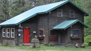 Eine Blockhütte mit roter Tür, Fenstern und einem Schild mit der Aufschrift 'Valdez Lodge'.