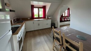 A compact kitchen with white cabinets, a wooden countertop, and a dining area with a table and chairs. - Les Fossiles - 4/6 people (Noyers-sur-Cher)