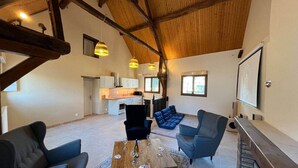 A spacious living area with a high ceiling, a fireplace, and a kitchen in the background. - Gite sleeps 18 (Noyers-sur-Cher)
