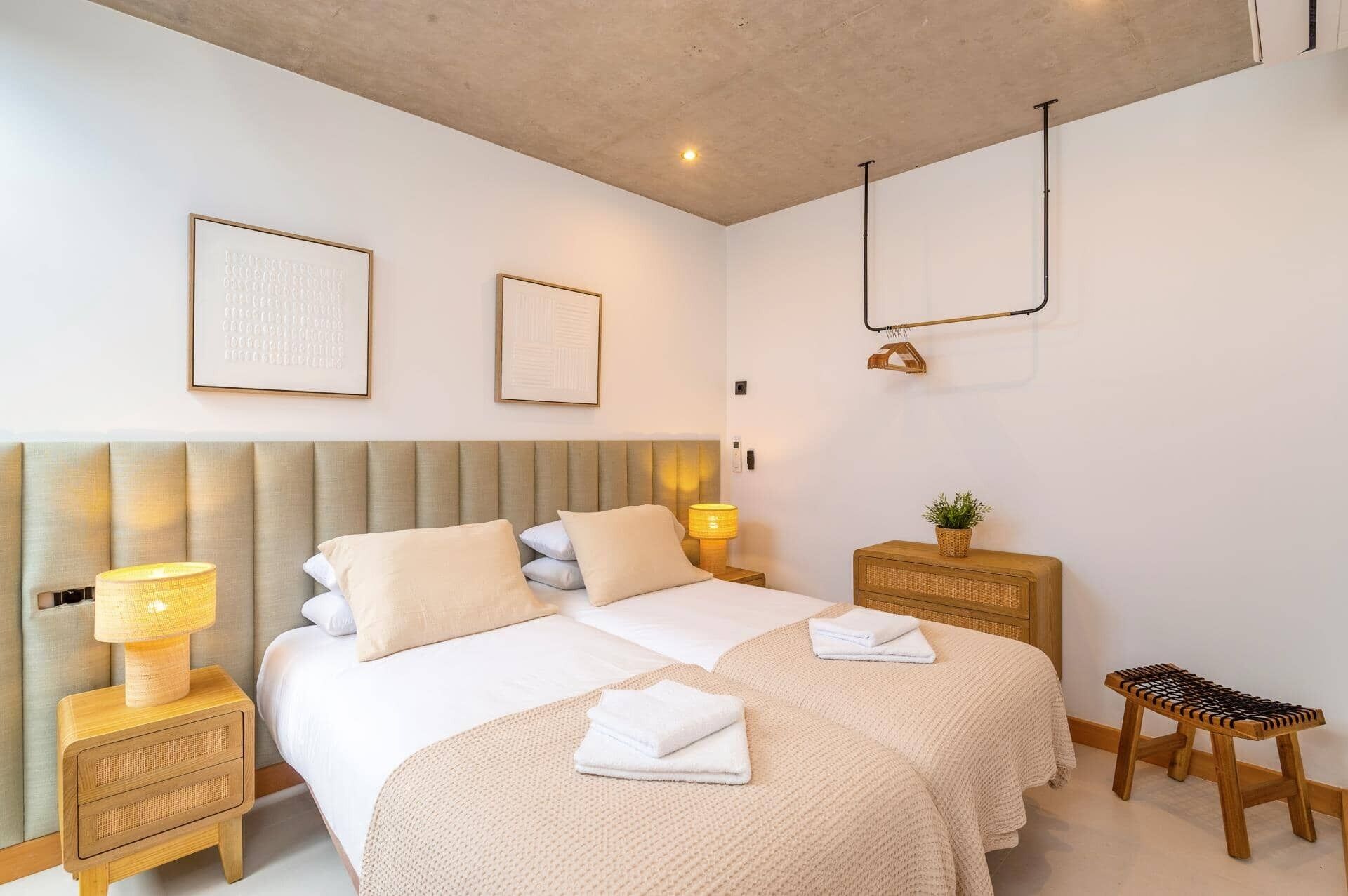 Een moderne slaapkamer met een groot bed, bedlampjes en een klein houten krukje.