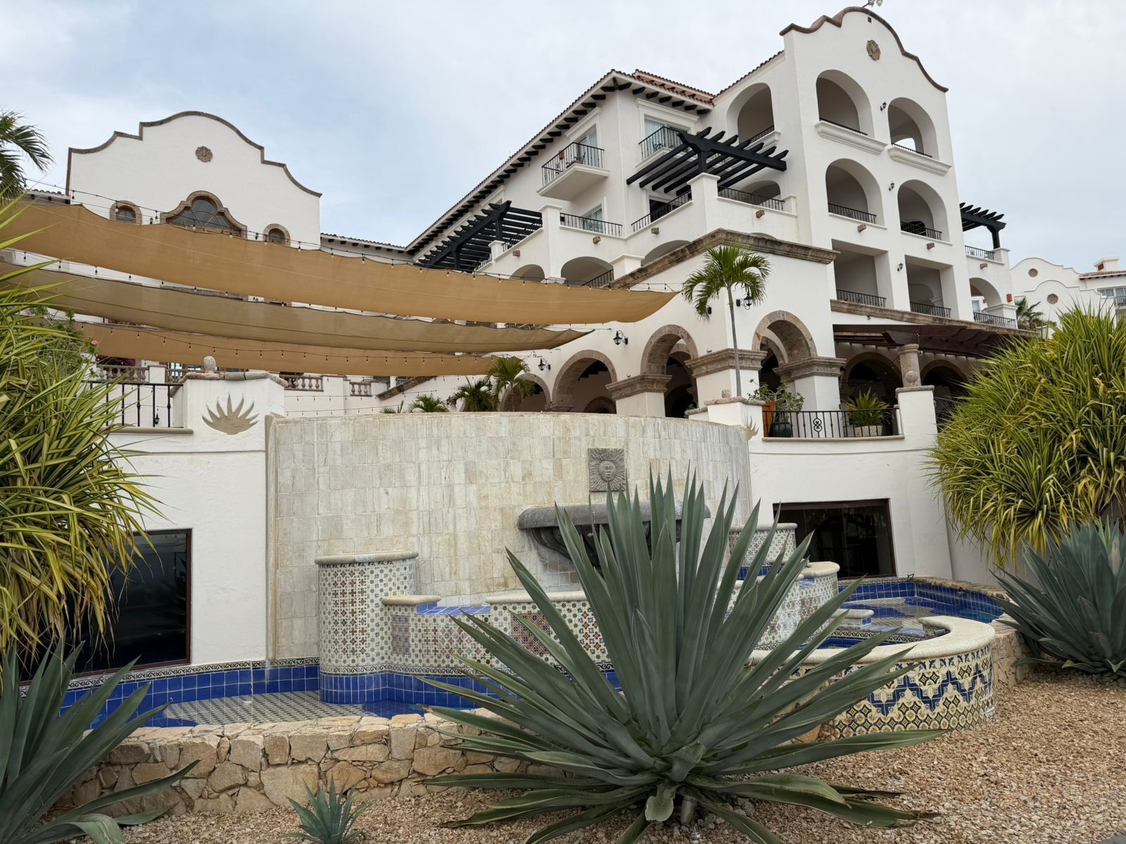 A hotel with a courtyard featuring a pool with blue mosaic tiles, surrounded by large agave plants.