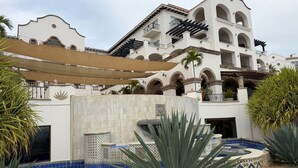 Un hotel con un patio que tiene una piscina con mosaicos azules, rodeada de grandes plantas de agave.