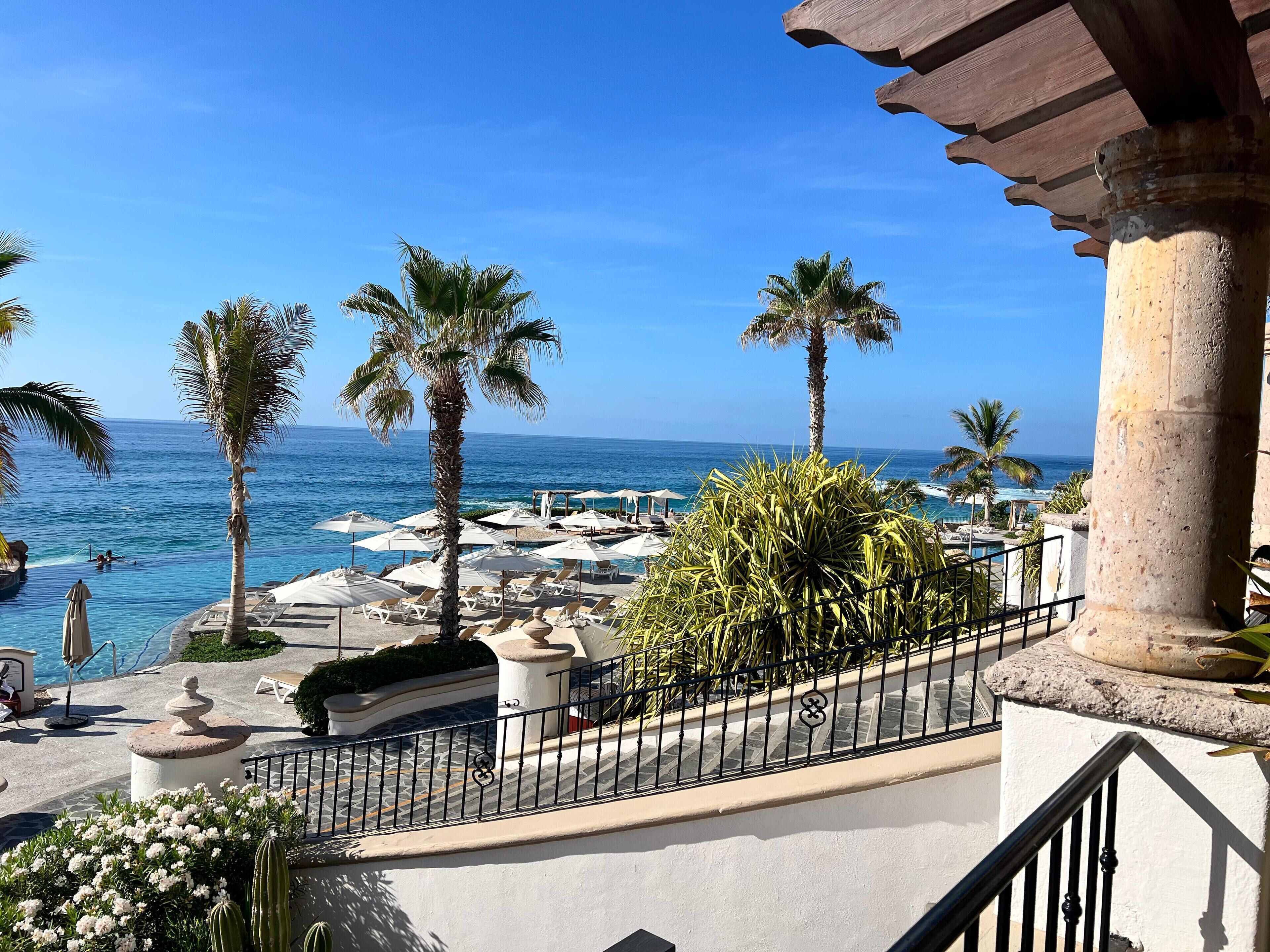 Un balcon d’hôtel avec vue sur l’océan, les palmiers et les chaises longues.
