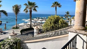 Balcón de un resort con vista al océano, palmeras y sillas de descanso.