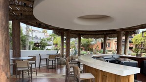 Zona de bar al aire libre con mobiliario de madera y una barra curva.