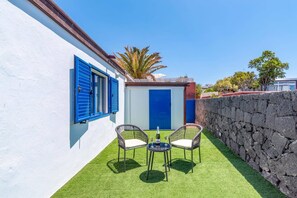 A courtyard with a white wall, a blue door, and a stone wall. There are two wicker chairs and a small table with a bottle and glasses. - Villa Lemes by Villa Plus (Playa Blanca)