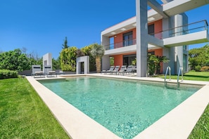 A modern pool area with clear water, lounge chairs, and a multi-story building with balconies. - Villa Kallisti Ialyssos by Villa Plus (Ialysos)
