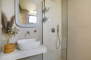 A bathroom with a white vessel sink, a mirror, a shower with a handheld showerhead, and a glass-enclosed shower. - Villa Kallisti Ialyssos by Villa Plus (Ialysos)