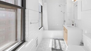 Een moderne badkamer met een groot raam, een douche, een wastafel en een spiegel.