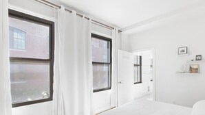 Een moderne slaapkamer met een groot bed, twee ramen, een deur en een klein plankje met decoratieve spullen.