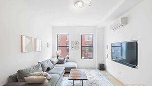 Een moderne woonkamer met een grijze bank, een salontafel en een grote flatscreen televisie aan de muur.